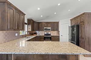 Kitchen featuring stainless steel appliances, vaulted ceiling, dark brown cabinetry, backsplash, and recessed lighting