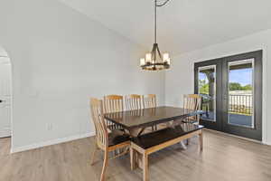 Dining area with lofted ceiling, french doors, light wood-style floors, arched walkways, and a chandelier