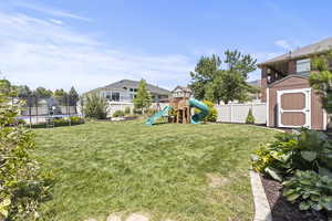 Fenced backyard featuring a trampoline, a shed, and a playground