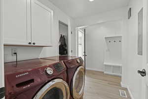 Laundry area with washing machine and clothes dryer, cabinet space, and light wood-style flooring