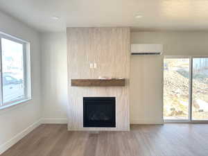 Detailed view of a large fireplace, wood finished floors, a wall mounted air conditioner, recessed lighting, and a textured ceiling