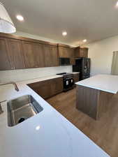 Kitchen featuring black appliances, backsplash, light wood-style flooring, a center island, and light stone counters