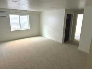Empty room featuring a textured ceiling, light colored carpet, and a wall unit AC