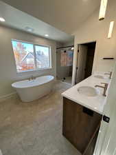 Full bath featuring a freestanding bath, double vanity, a shower stall, vaulted ceiling, and recessed lighting