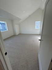 Additional living space featuring light carpet and vaulted ceiling