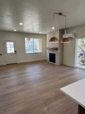 Unfurnished living room featuring plenty of natural light, a textured ceiling, a fireplace, light wood finished floors, and recessed lighting