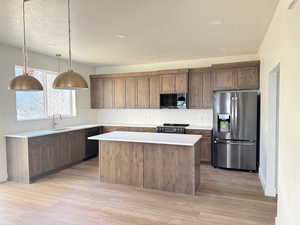 Kitchen with black appliances, a kitchen island, backsplash, hanging light fixtures, and a textured ceiling