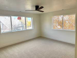 Empty room featuring light colored carpet, a textured ceiling, and a ceiling fan