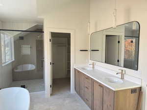 Full bathroom featuring a freestanding tub, a shower stall, double vanity, a textured ceiling, and a walk in closet