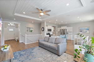 Living room featuring a tray ceiling, light wood-type flooring, ceiling fan, recessed lighting, and a chandelier