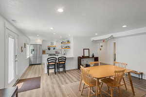 Dining room with a textured ceiling, light wood-type flooring, and recessed lighting