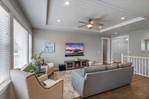 Living room featuring a raised ceiling, wood finished floors, recessed lighting, and ceiling fan