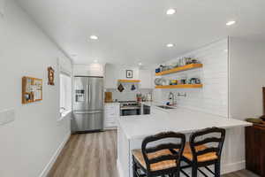 Kitchen with appliances with stainless steel finishes, light wood-type flooring, decorative backsplash, a peninsula, and recessed lighting