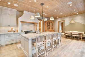 Kitchen featuring wooden ceiling, a center island with sink, white cabinetry, stove, and light wood-style floors