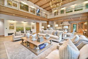 Living room featuring a wood ceiling with exposed beams, a high ceiling, wood finished floors, a chandelier, and recessed lighting