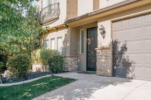 Entrance to property featuring a garage, stucco siding, stone siding, and a balcony