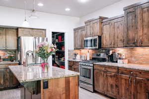 Kitchen featuring stainless steel appliances, light stone countertops, light wood-style floors, tasteful backsplash, and a kitchen island