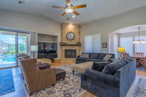 Living area with light wood finished floors, arched walkways, a chandelier, a ceiling fan, and vaulted ceiling