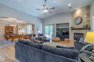 Living room featuring wood finished floors, pool table, a fireplace, arched walkways, and vaulted ceiling