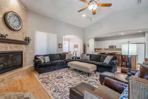 Living room featuring arched walkways, lofted ceiling, light wood-type flooring, ceiling fan, and a premium fireplace