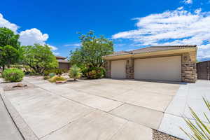 View of front of property featuring stone siding, driveway, an attached 3 car garage, and a tiled roof