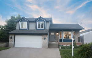 Tri-level home featuring stone siding, a garage, and concrete driveway