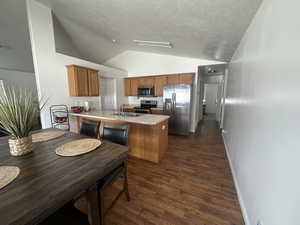 Kitchen with appliances with stainless steel finishes, a peninsula, dark wood-style floors, lofted ceiling, and brown cabinetry