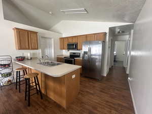 Kitchen with stainless steel appliances, a peninsula, lofted ceiling, dark wood-style flooring, and brown cabinets