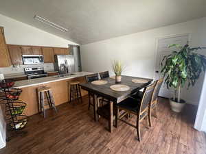 Dining room featuring vaulted ceiling, dark wood-style floors, and a textured ceiling