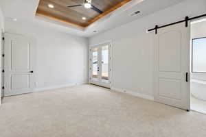 Unfurnished bedroom with a tray ceiling, access to outside, multiple windows, a barn door, and wooden ceiling