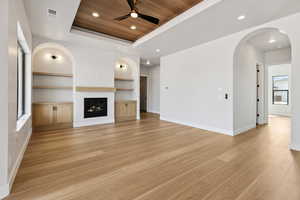 Unfurnished living room with a raised ceiling, a ceiling fan, built in features, light wood finished floors, and wood ceiling