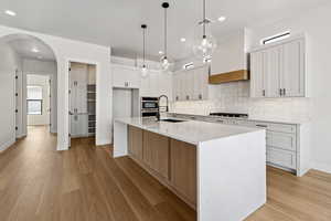 Kitchen featuring gas cooktop, arched walkways, backsplash, recessed lighting, and light wood-style floors
