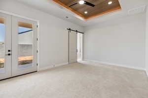 Carpeted spare room featuring a raised ceiling, a ceiling fan, a barn door, recessed lighting, and healthy amount of natural light