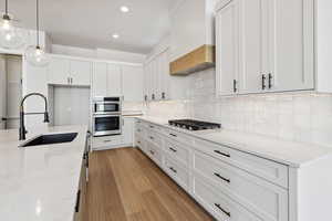 Kitchen featuring stainless steel appliances, custom exhaust hood, white cabinets, backsplash, and recessed lighting