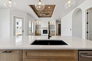 Kitchen with open floor plan, a fireplace, dishwasher, light stone countertops, and pendant lighting