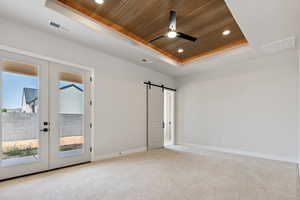 Empty room with a tray ceiling, wood ceiling, a barn door, ceiling fan, and recessed lighting