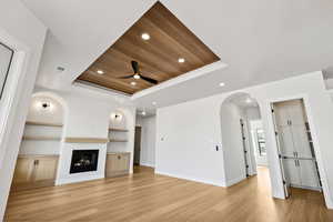 Unfurnished living room with a tray ceiling, a ceiling fan, wood ceiling, light wood finished floors, and built in shelves