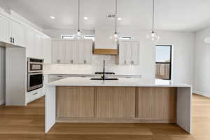 Kitchen featuring tasteful backsplash, a spacious island, white cabinets, light countertops, and recessed lighting