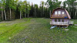 Back of property with a gambrel roof, a deck, a yard, and a forest view