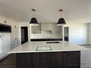 Kitchen with stainless steel microwave, a kitchen island with sink, light countertops, a textured ceiling, and wood finished floors