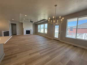 Unfurnished living room with a textured ceiling, light wood-style flooring, a ceiling fan, a chandelier, and recessed lighting