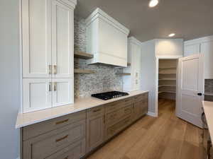 Kitchen with stainless steel gas stovetop, light wood-style flooring, gray cabinets, open shelves, and backsplash