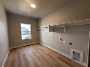 Laundry area featuring electric dryer hookup, hookup for a washing machine, light wood-style flooring, and a textured ceiling