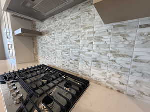 Kitchen view of stainless steel gas stovetop, decorative backsplash, open shelves, and range hood