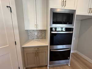Kitchen featuring stainless steel appliances, tasteful backsplash, light wood finished floors, light stone countertops, and white cabinetry
