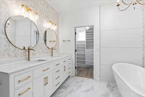 Bathroom with a chandelier, double vanity, a freestanding bath, marble look tile flooring, and a walk in closet