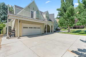 View of side of property with a balcony, concrete driveway, a shingled roof, an attached garage, and a yard