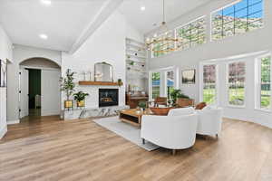 Living area featuring light wood-style floors, high vaulted ceiling, a fireplace, plenty of natural light, and recessed lighting