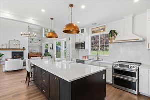 Kitchen with stainless steel appliances, premium range hood, white cabinetry, light countertops, and wood finished floors