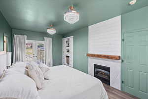 Bedroom featuring wood finished floors, a fireplace, access to exterior, a chandelier, and french doors